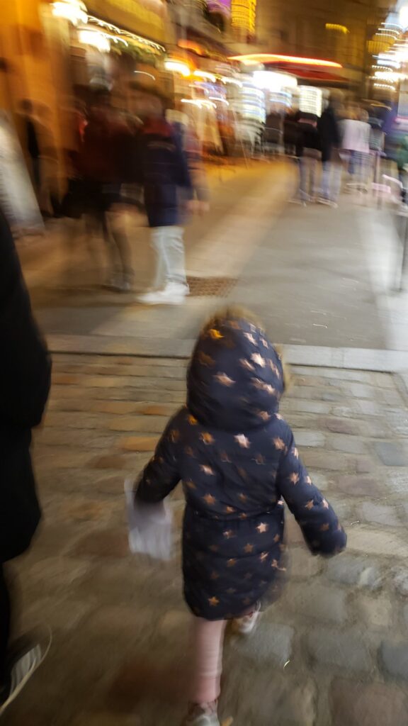 Our daughter in a winter coat, seen from behind, walking through Paris, France on a December evening
