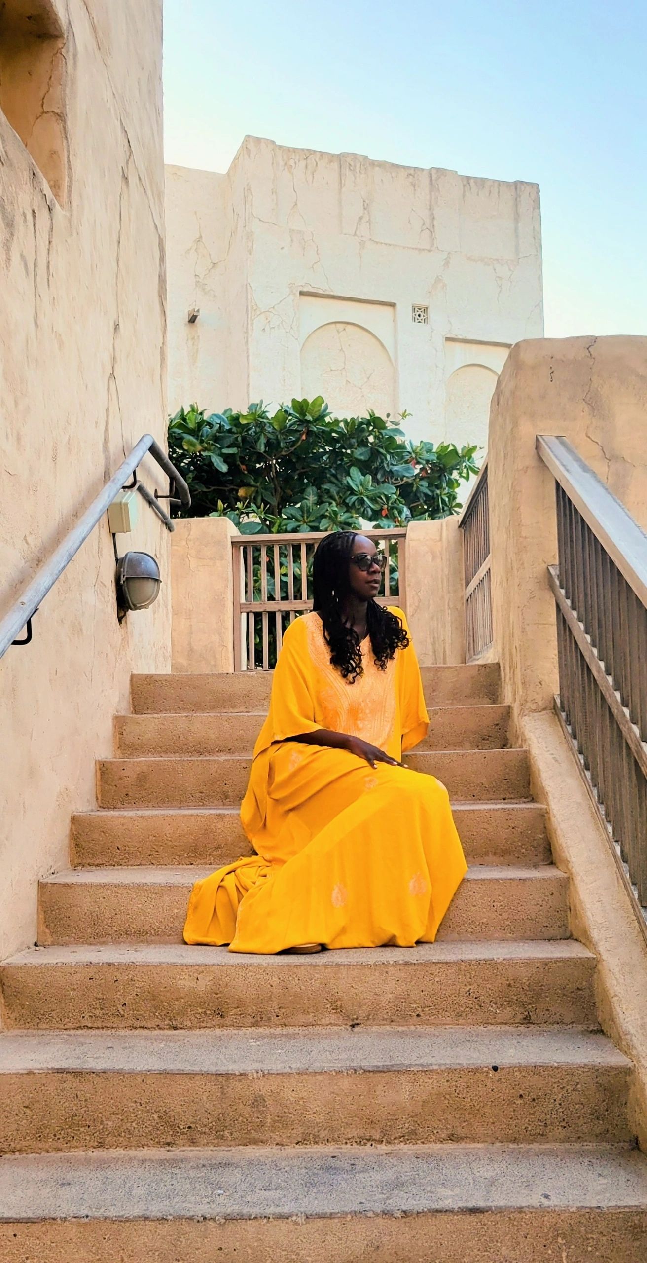 Samira Diallo of Mayana Voyage in a yellow dress on stone stairs